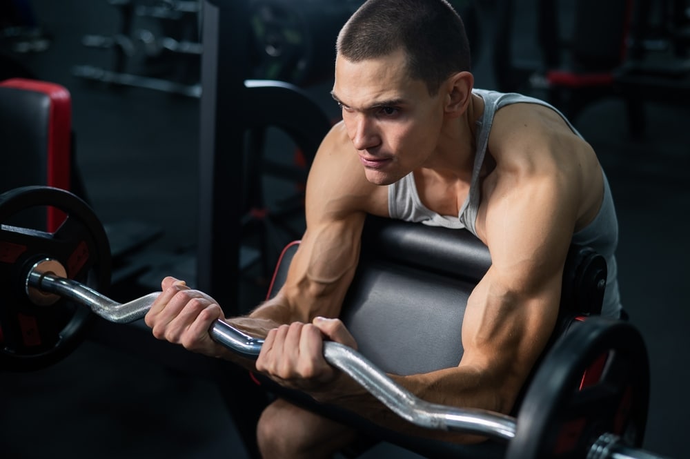 Man Doing Ez Barbell Bicep Exercises On Scott Bench