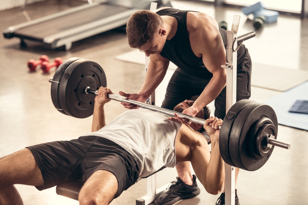 Athletic Trainer Helping Sportsman Lifting Barbell With Heavy Weight Plates