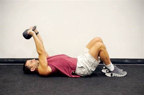 a man is lay down on a floor and doing Kettlebell Skull Crushers exercise