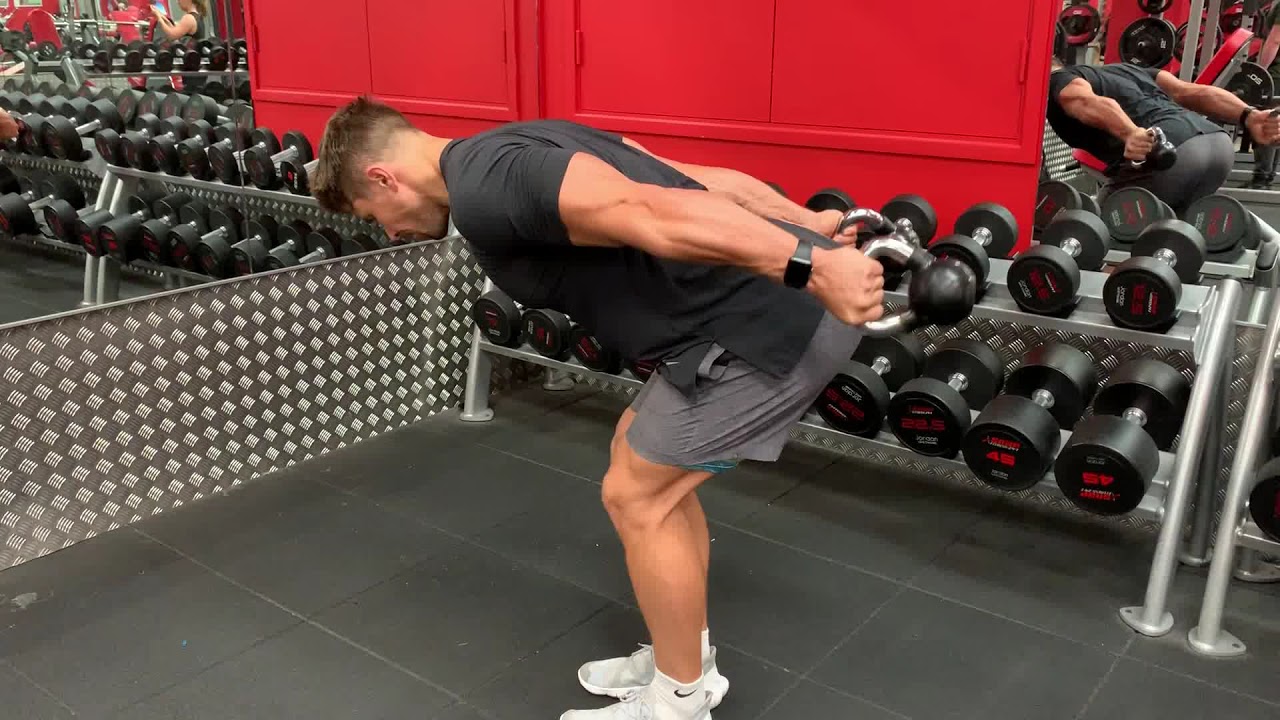 a man is doing Kettlebell Tricep Kickbacks exercise in gynm along with dumbells on side