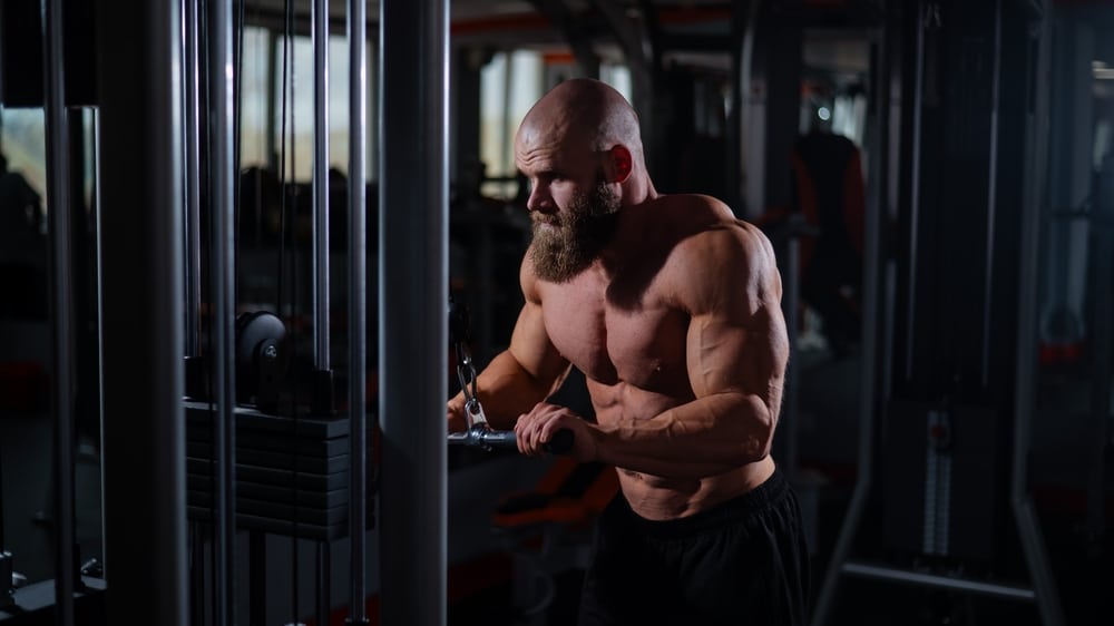 Bald Caucasian Bodybuilder Doing Heavy Triceps Exercises With Cable